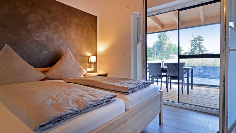 Ein modernes Schlafzimmer mit einem Doppelbett und einer gemütlichen Atmosphäre. Das Zimmer hat einen Zugang zu einer Terrasse mit Blick ins Freie.