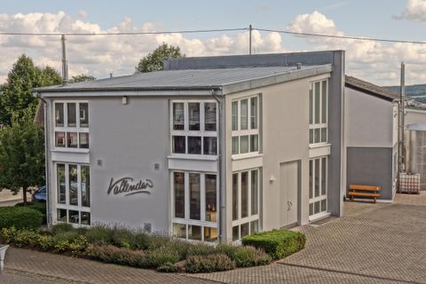 Ein modernes Gebäude mit großen Fenstern und einem grauen Außenanstrich. Es ist von einem gepflegten Landschaftsbereich umgeben.