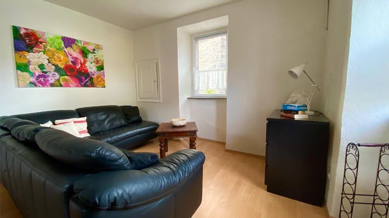 Ein gemütliches Wohnzimmer mit einer schwarzen Ledercouch und einem kleinen Tisch. An der Wand hängt ein farbenfrohes Gemälde.