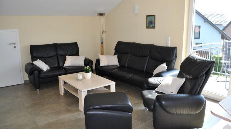 Ein modernes Wohnzimmer mit schwarzen Ledermöbeln und einem hellen Tisch. Große Fenster sorgen für viel Tageslicht und eine freundliche Atmosphäre.