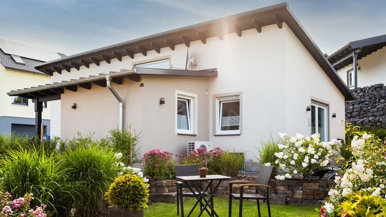 Ein modernes Haus mit einem schönen Garten. Im Vordergrund stehen zwei Stühle und ein kleiner Tisch.