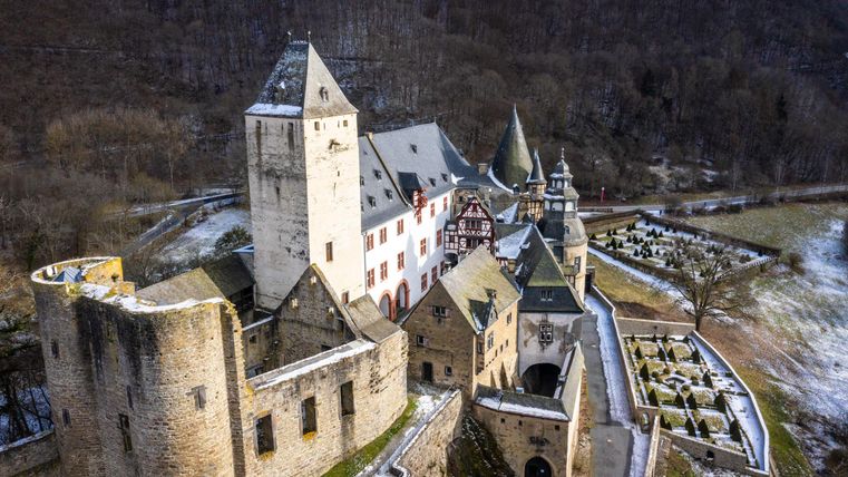 Eine wunderschöne Burg in einer winterlichen Landschaft. Die Anlage zeigt historische Architektur und umliegende Felder.