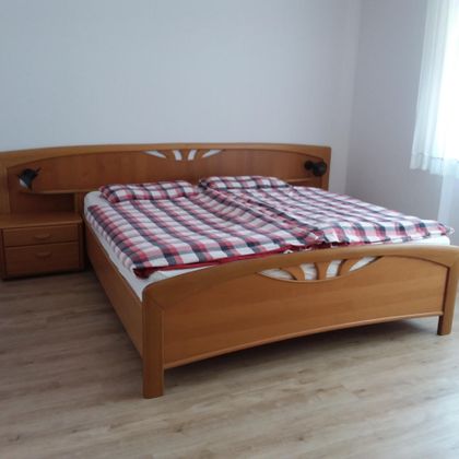 Ein Schlafzimmer mit einem großen Holzbett und karierten Betttüchern. Neben dem Bett steht ein kleiner Nachttisch.