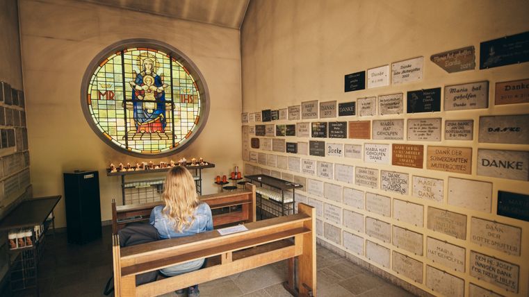 Der Innenraum einer kleinen Kapelle. Eine Person sitzt auf einer Holzbank. 