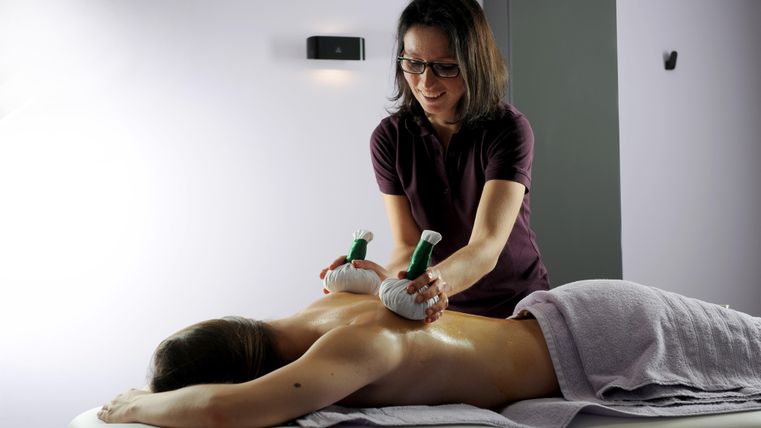 Eine Frau erhält eine Massage mit speziellen Geräten. Die Therapeutin konzentriert sich auf den oberen Rücken des Klienten.