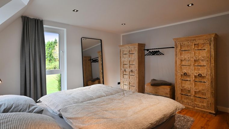 Ein gemütliches Schlafzimmer mit einem Doppelbett und zwei Holzkleiderschränken. Großes Fenster mit Blick ins Grüne und moderne Einrichtung.