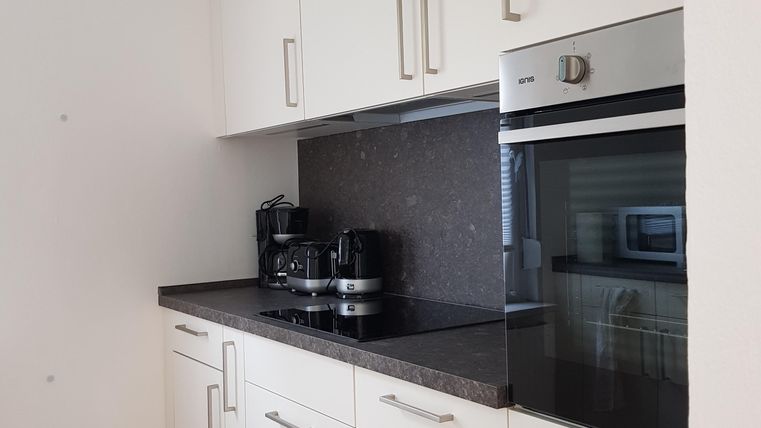 Eine moderne Küche mit weißen Schränken und einer dunklen Arbeitsplatte. Es gibt Küchengeräte wie einen Kaffeeautomaten und einen Backofen.