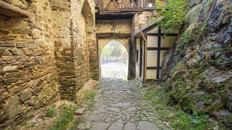 Ein malerischer Weg mit Steinen, der zu einem Tor führt. Umgeben von alten Steinmauern und üppigem Grün.