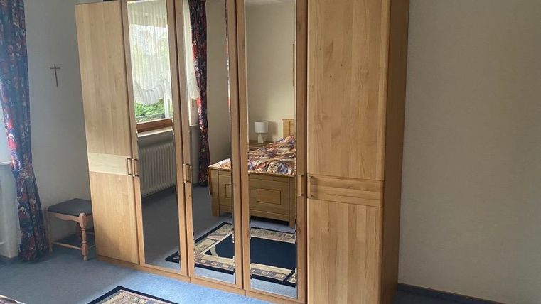 Ein Schlafzimmer mit einem großen Holzschrank und Spiegeln. Der Raum ist einfach eingerichtet mit einem Bett und einem Teppich.