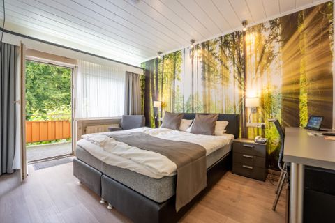 Ein Hotelzimmer mit einem Bett, dahinter eine Tapete mirt Waldmotiv