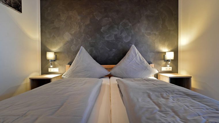 Ein gemütliches Schlafzimmer mit zwei Einzelbetten und Nachtlichtern. Die Wände sind in einem dunklen Farbton gestaltet.