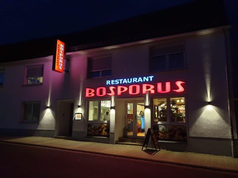 Ein Restaurant mit dem Namen "Bosporus" leuchtet bunt in der Nacht. Die Fassade ist freundlich und einladend.