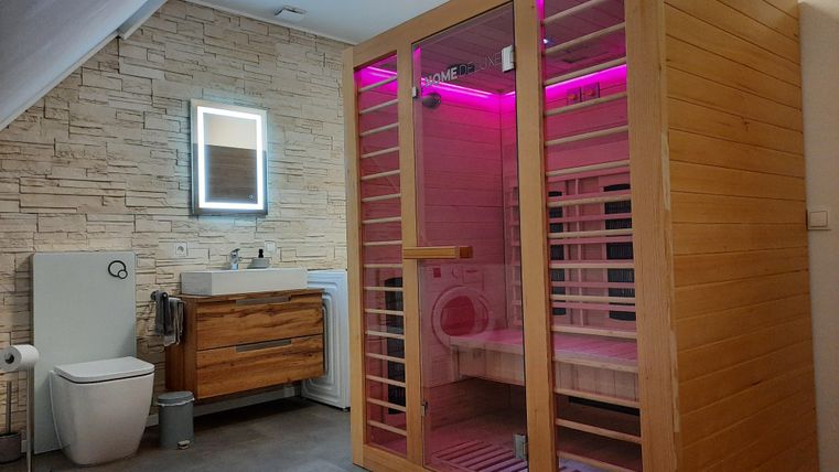 Ein modernes Badezimmer mit einer Holzsauna und farbiger LED-Beleuchtung. Im Hintergrund sind ein Waschbecken und eine Toilette zu sehen.