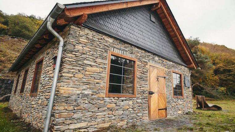 Ein charmantes Steinhaus mit einem Holzdach. Es steht in einer natürlichen Umgebung mit Bäumen im Hintergrund.