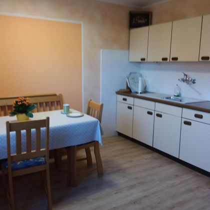 Eine gemütliche Küche mit einem Essbereich und einem Tisch. Die Wände sind in warmen Farben gestrichen, und die Möbel sind aus Holz.