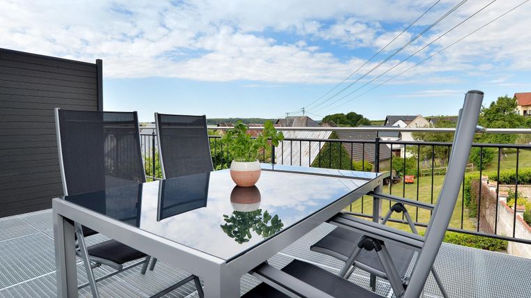 Ein moderner Tisch mit Stühlen auf einer Terrasse. Im Hintergrund sind Häuser und ein blauer Himmel zu sehen.