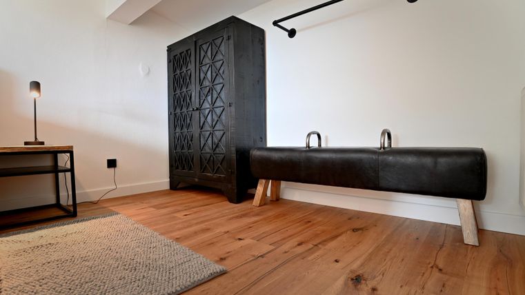 Eine moderne Inneneinrichtung mit einem schwarzen Schrank und einer schlichten Bank. Der Boden ist aus hellem Holz, und es gibt einen kleinen Teppich.