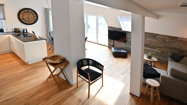 Ein modernes Wohnzimmer mit einem offenen Küchenbereich. Helle Holzböden und große Fenster sorgen für eine angenehme Atmosphäre.