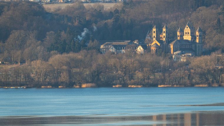 Eine malerische Landschaft mit einem ruhigen See und einer historischen Kirche im Hintergrund. Die Bäume und die sanfte Hügellandschaft schaffen eine friedliche Atmosphäre.