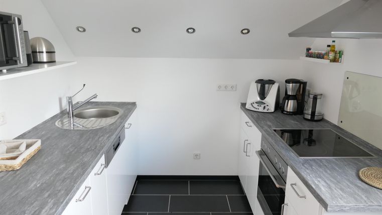 Een moderne keuken met een grijs werkblad en witte kasten. Ze is goed uitgerust met apparaten zoals een fornuis en een koffiezetter.