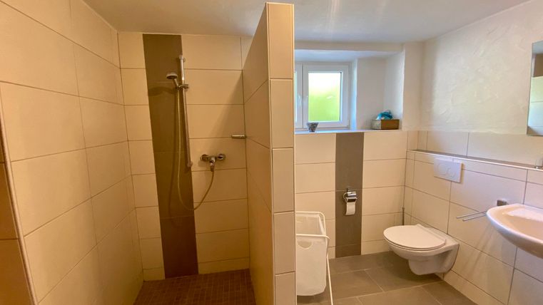 Ein modernes Badezimmer mit einer Dusche und einer Toilette. Die Wände sind hell gefliest und es gibt ein Fenster, das Tageslicht hereinscheinen lässt.