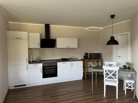 Een moderne keuken met witte meubels en een eettafel. Er zijn keukentoestellen zoals een fornuis en een magnetron zichtbaar.