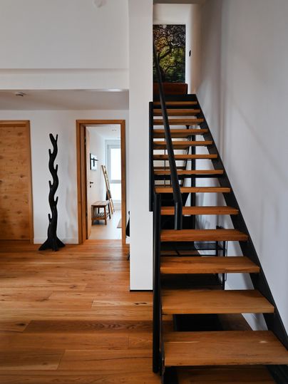Eine moderne Treppe aus Holz führt nach oben. Der Boden ist aus hellem Holz und der Raum wirkt offen und einladend.