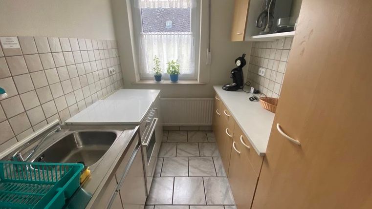 Eine kleine Küche mit hellen Fliesen und einer Spüle. Auf der Arbeitsfläche stehen Pflanzen und kleine Küchengeräte.