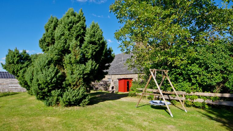 Ein schöner Garten mit großen grünen Bäumen und einer Schaukel. Im Hintergrund ist ein charmantes Gebäude mit einer roten Tür zu sehen.