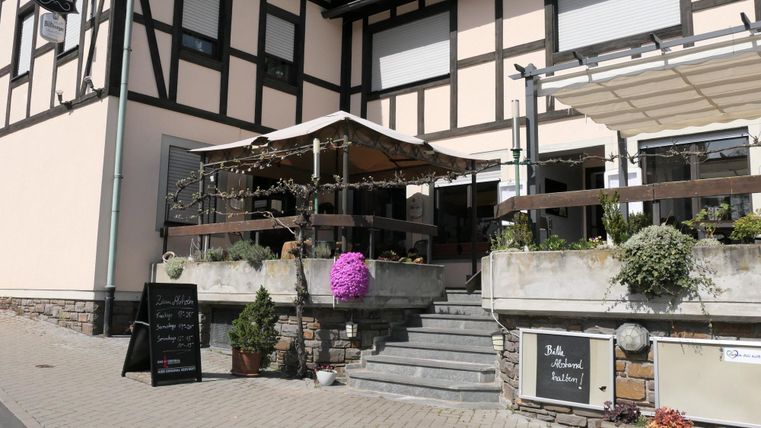 Ein charmantes Restaurant mit einem überdachten Außenbereich und schönen Pflanzen. Die Fassade zeigt ein traditionelles Fachwerkdesign.