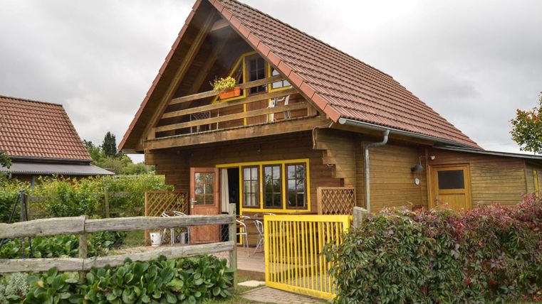 Une maison en bois confortable avec un toit rouge et un balcon. Le jardin est vert et bien entretenu, et il y a une clôture en bois.