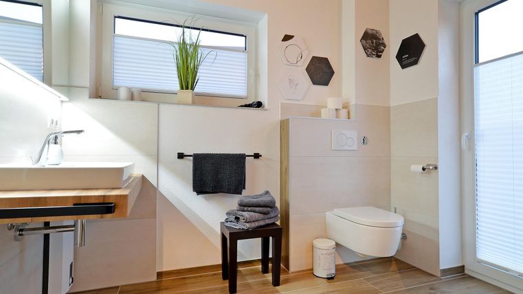 Ein modernes Badezimmer mit einem eleganten Waschtisch und einem WC. Große Fenster lassen viel Licht herein und es gibt dekorative Akzente an den Wänden.