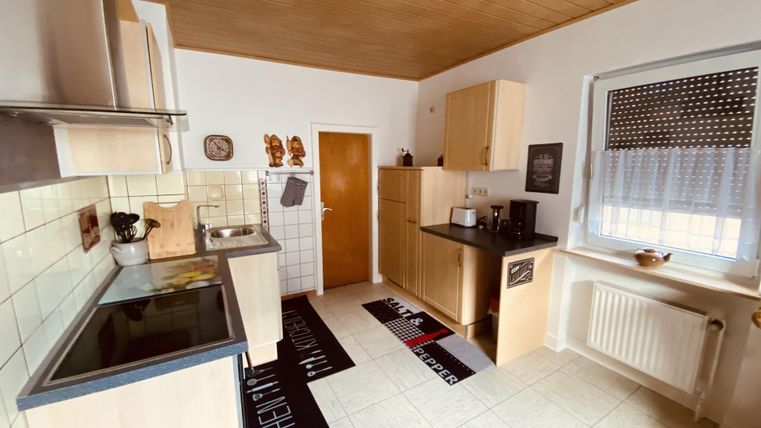 Eine moderne Küche mit hellen Holzschränken und einer hellen Wand. Der Raum ist gut beleuchtet und verfügt über moderne Küchengeräte.