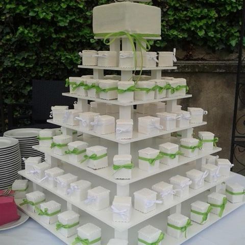 Eine elegante Tortenkreation auf mehreren Ebenen mit kleinen, weißen Kästchen, die mit grünen Bändern dekoriert sind. Im Hintergrund sind Teller zu sehen.