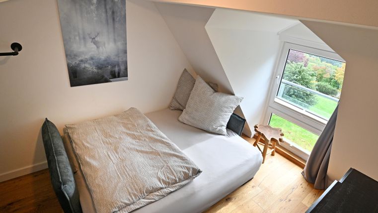 Ein gemütliches Schlafzimmer mit einem Fenster und Blick auf den Garten. Die Möbel sind modern und die Wand ist mit einem Bild dekoriert.