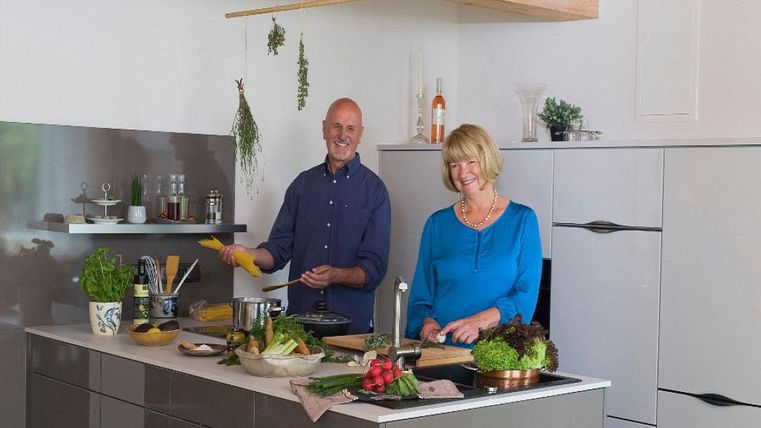 Un couple amical cuisine dans une cuisine moderne.
Des légumes frais sont disposés sur le plan de travail, et l'atmosphère est accueillante et détendue.