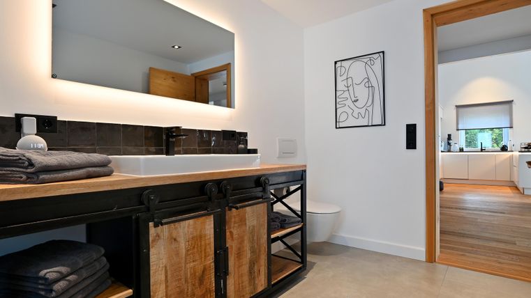 Ein modernes Badezimmer mit einem Holzwaschtisch und einem großen Spiegel. Im Hintergrund ist ein weiteres Zimmer sichtbar.