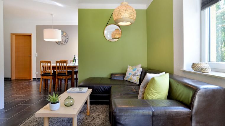 Ein modernes Wohnzimmer mit einer gemütlichen Couch und einem Holzkaffeetisch. Die Wände sind in einem frischen Grünton gestrichen und es gibt viel Tageslicht.