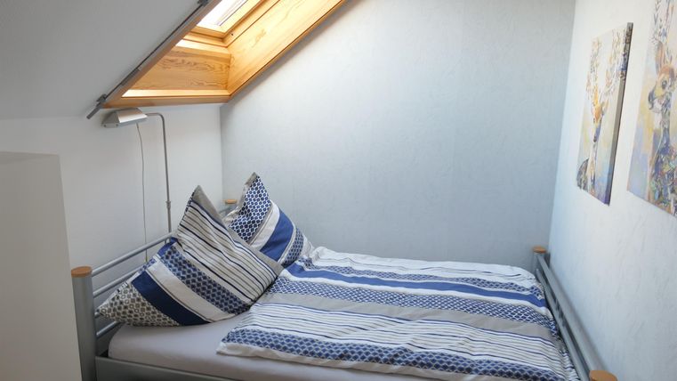 Een gezellige slaapkamer met een dakraam. Het bed is versierd met kussens in blauw- en grijstinten.