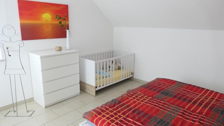 Een slaapkamer met een kinderbed en een witte kast. Aan de muur hangt een schilderij met een zonsondergang.