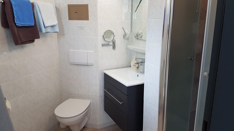 Ein modernes Badezimmer mit einem Waschbecken, Spiegel und Toilette. Handtücher in verschiedenen Farben hängen an der Wand.