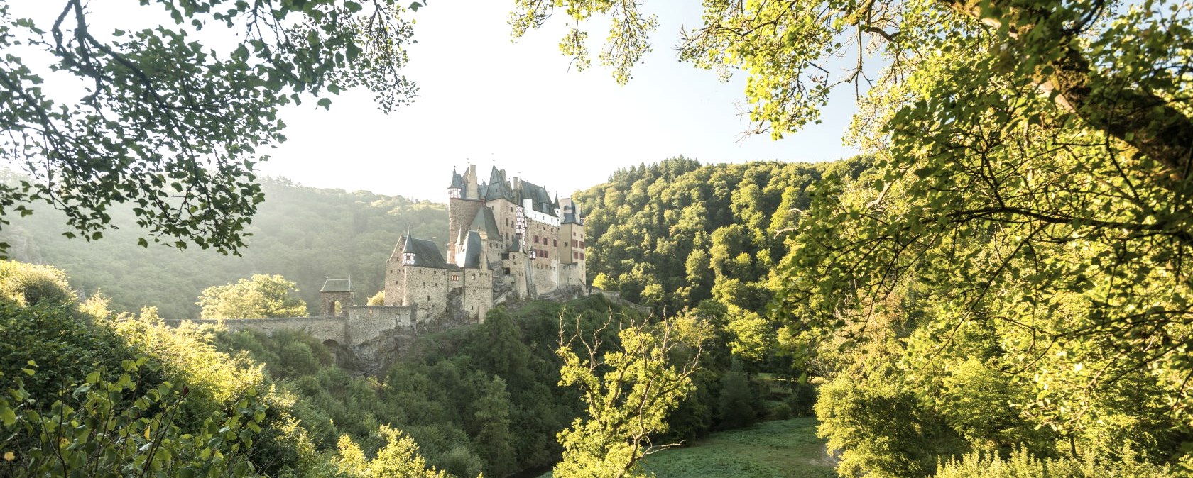 Burg Eltz thront majest&auml;tisch auf einem H&uuml;gel, umgeben von &uuml;ppigem Gr&uuml;n und beleuchtet von warmem Sonnenlicht. Ein malerischer Anblick., &copy; Rheinland-Pfalz Tourismus GmbH, D. Ketz