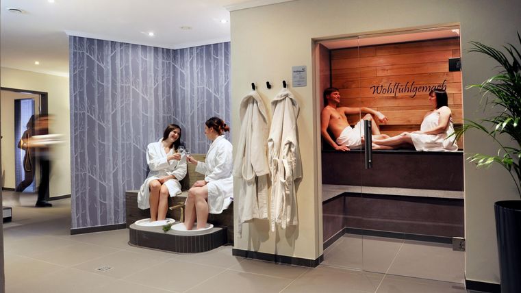 Ein entspannender Spa-Bereich mit angenehmer Beleuchtung. Zwei Gäste genießen eine Behandlung, während andere im Hintergrund relaxen.