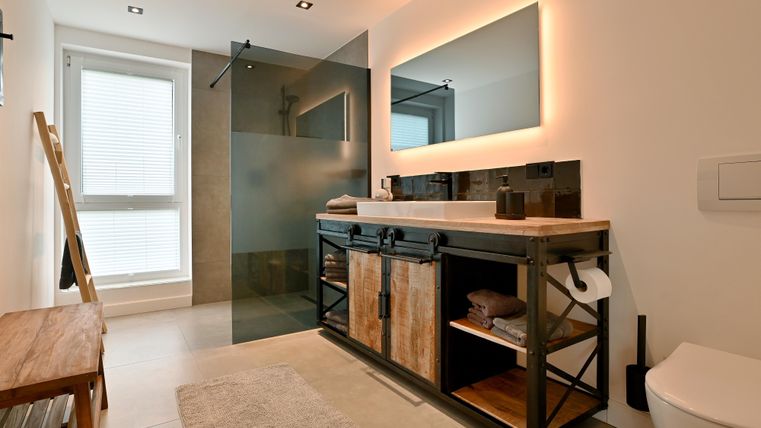 Ein modernes Badezimmer mit einer großen Duschkabine und einem eleganten Waschtisch. Die warme Beleuchtung sorgt für eine gemütliche Atmosphäre.