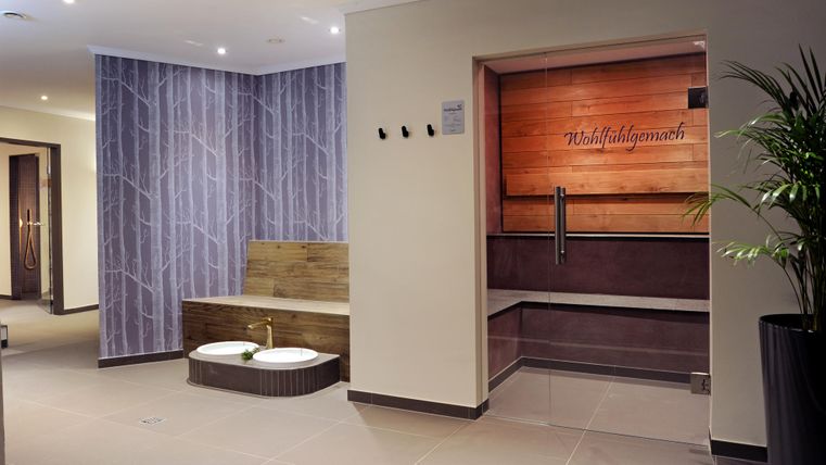 Ein modernes Spa mit angenehmem Ambiente. Zu sehen sind Sitzgelegenheiten und entspannende Elemente wie Pflanzen und Holzverkleidungen.