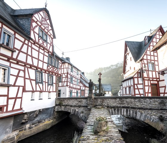 Fachwerkhäuser in Monreal mit einer steinernen Brücke über einen kleinen Fluss. Eine Statue steht auf der Brücke., © Eifel Tourismus GmbH, D. Ketz