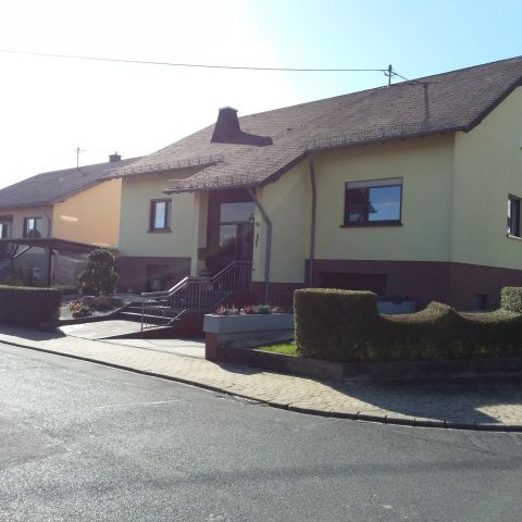 Ein einladendes Haus mit gelber Fassade und einem davorliegenden Garten. Die Straße verläuft sanft um die Ecke des Grundstücks.