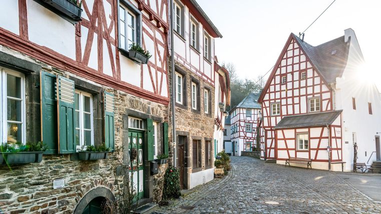 Ein malerischer Dorfweg mit historischen Fachwerkhäusern. Die Sonne scheint auf die gepflasterte Straße und die grüne Fensterläden.