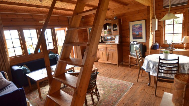 Une maison en bois confortable avec un espace de vie ouvert. On peut voir un escalier, un coin cuisine et plusieurs sièges.