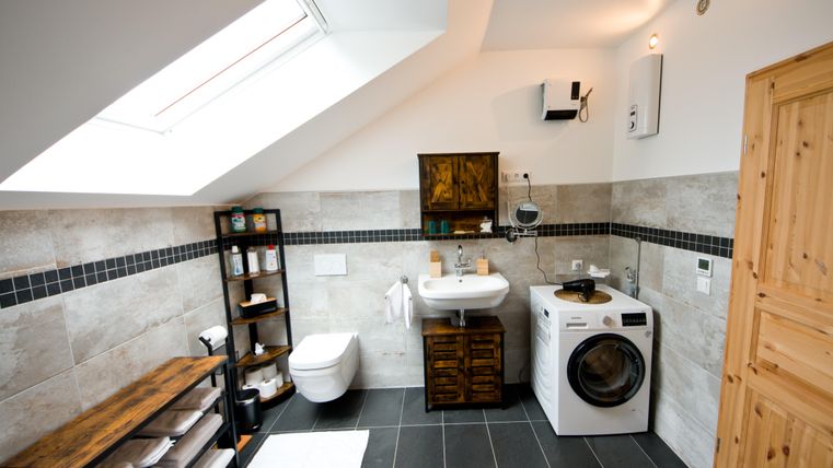 Ein modernes Badezimmer mit einem Fenster im Dach. Es gibt eine Waschmaschine, ein Waschbecken und Holzregale.